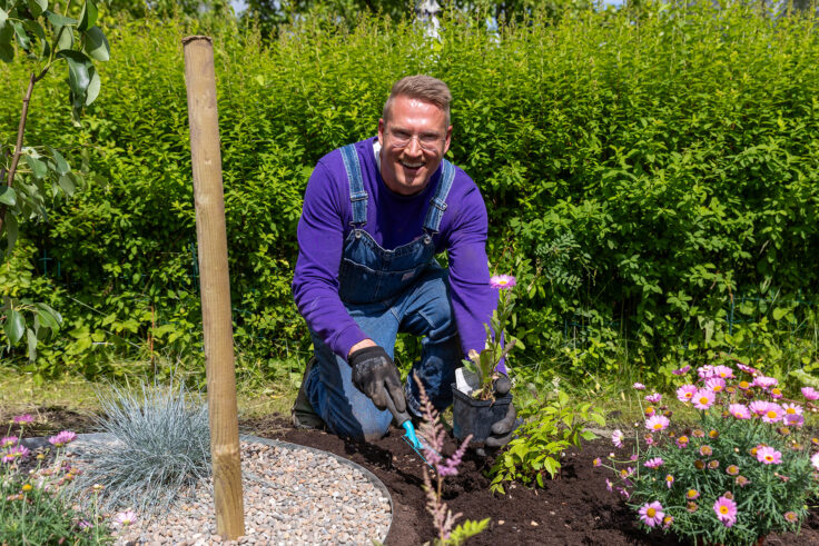 Puutarhuri Jussi Petäjä istuttaa kukkia ja perennoja siirtolapuutarhan kukkapenkkiin aurinkoisena kesäpäivänä.